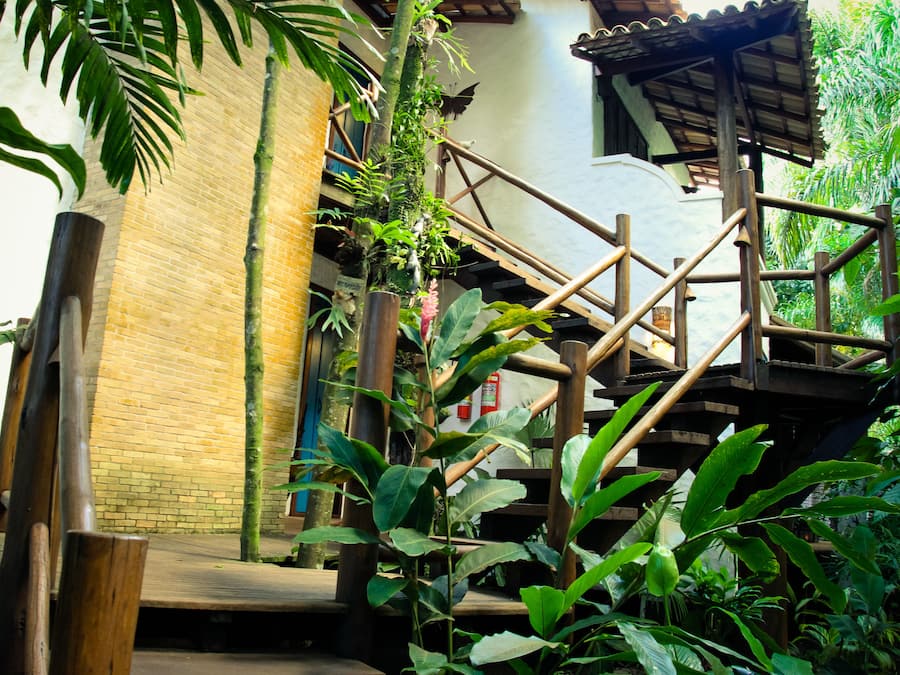 Una escalera de madera junto a un muro de ladrillo y abundante vegetación.