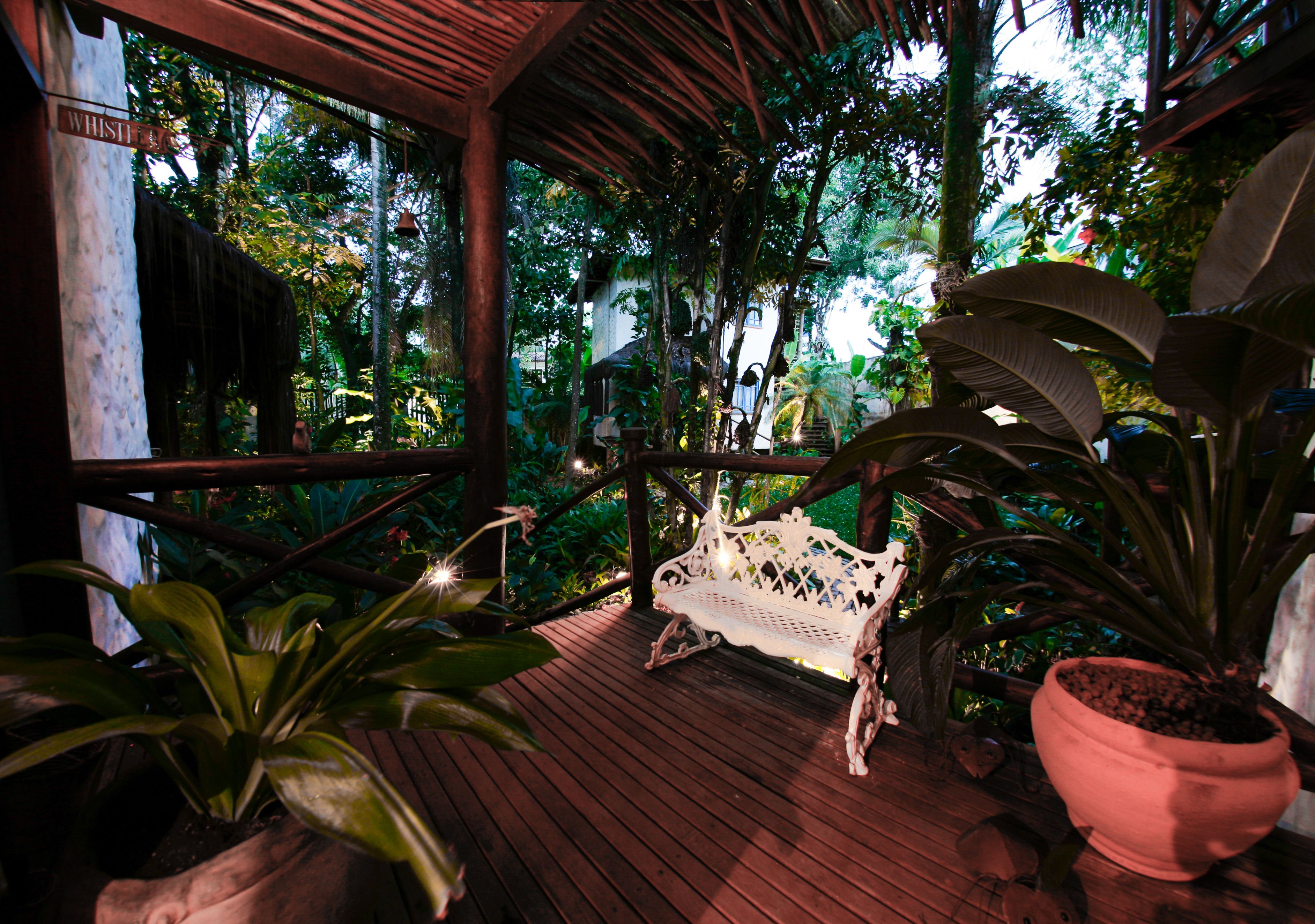 A wooden deck with a white bench, surrounded by lush greenery and a wooden railing.