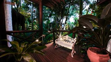 A wooden deck with a white bench, surrounded by lush greenery and a wooden railing.