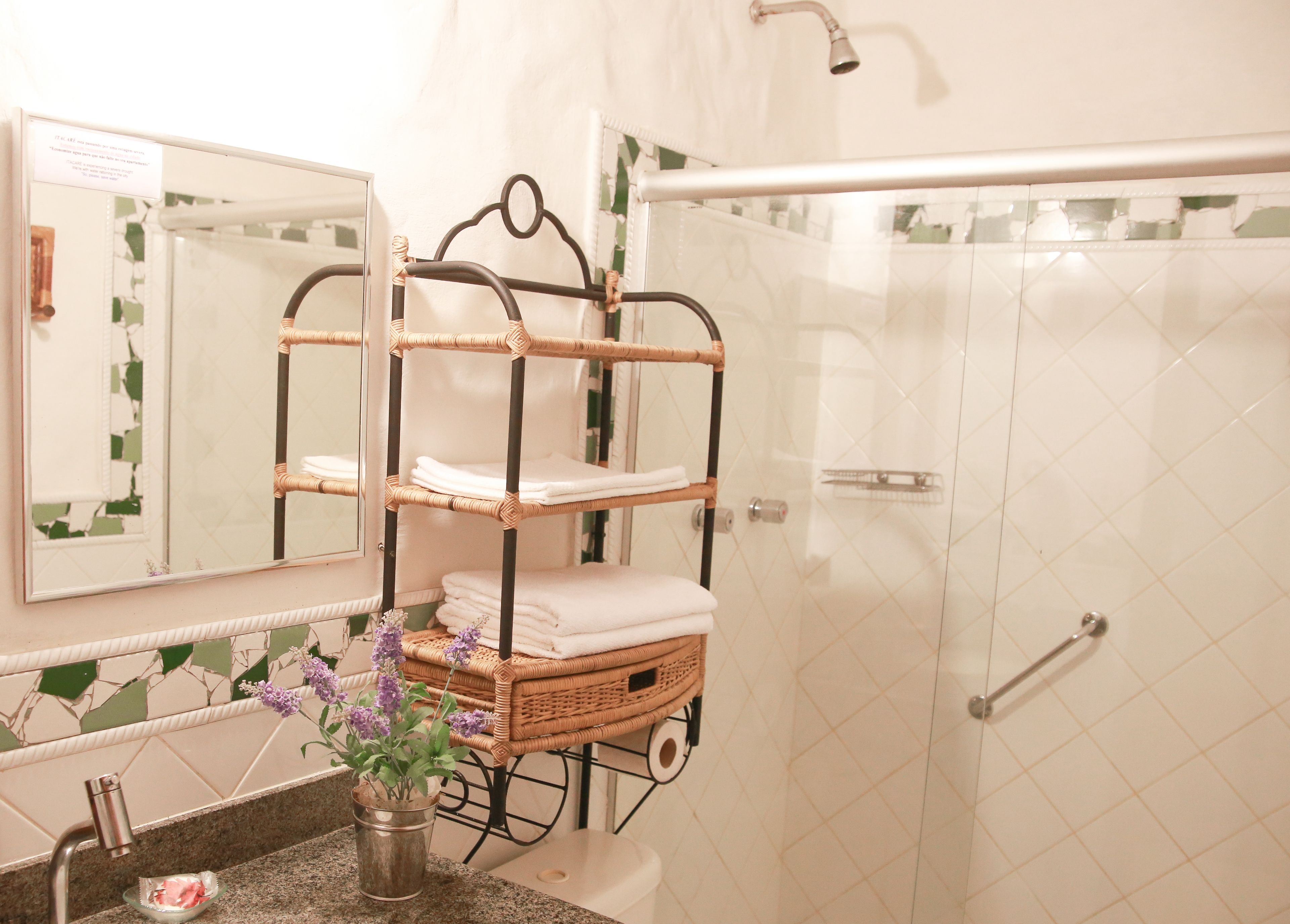 Un baño con un estante de mimbre de tres niveles que contiene toallas, un espejo y una planta en maceta.