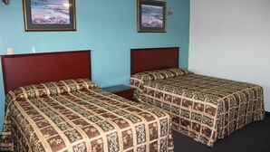 A room with two beds, each with a patterned bedspread, a wooden headboard, and a small bedside table. There are two framed pictures on the wall. - Sportsman Motel (Eagle Lake)