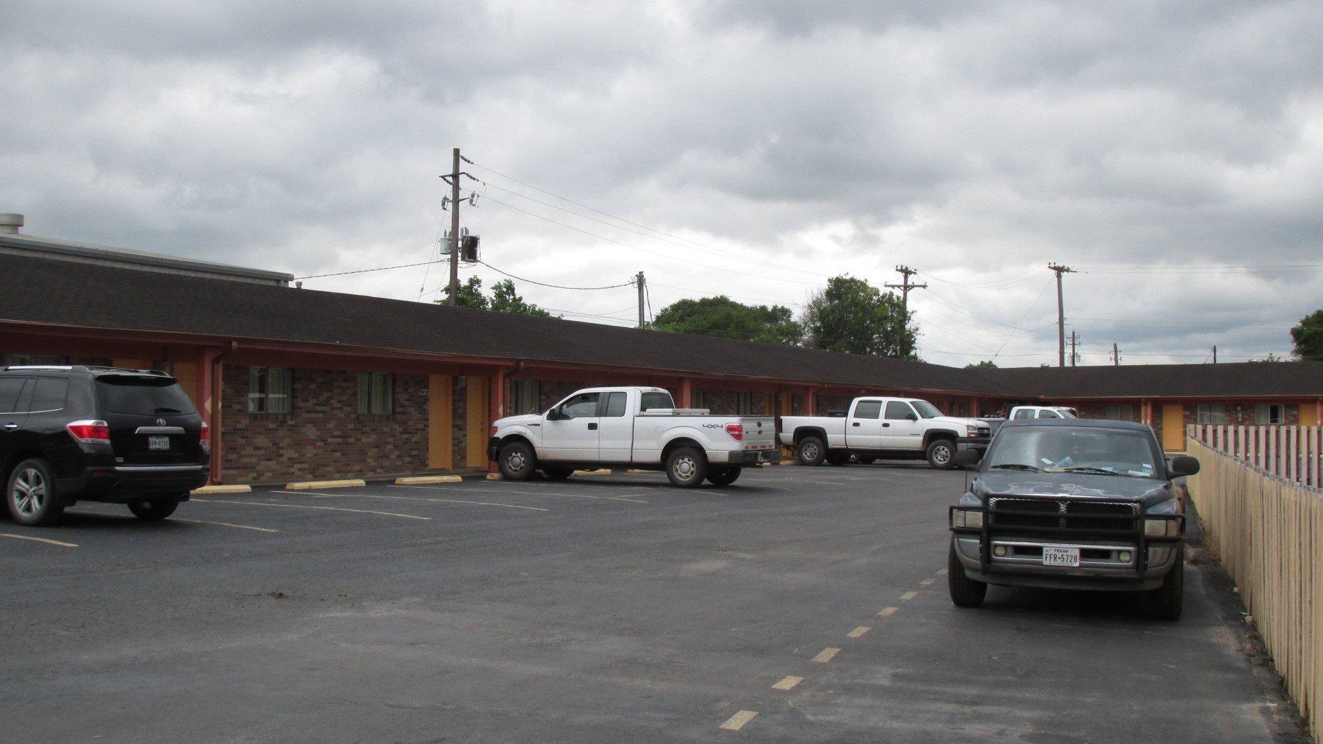 Un motel con estacionamiento, varios vehículos estacionados y un edificio de ladrillo con techo plano.