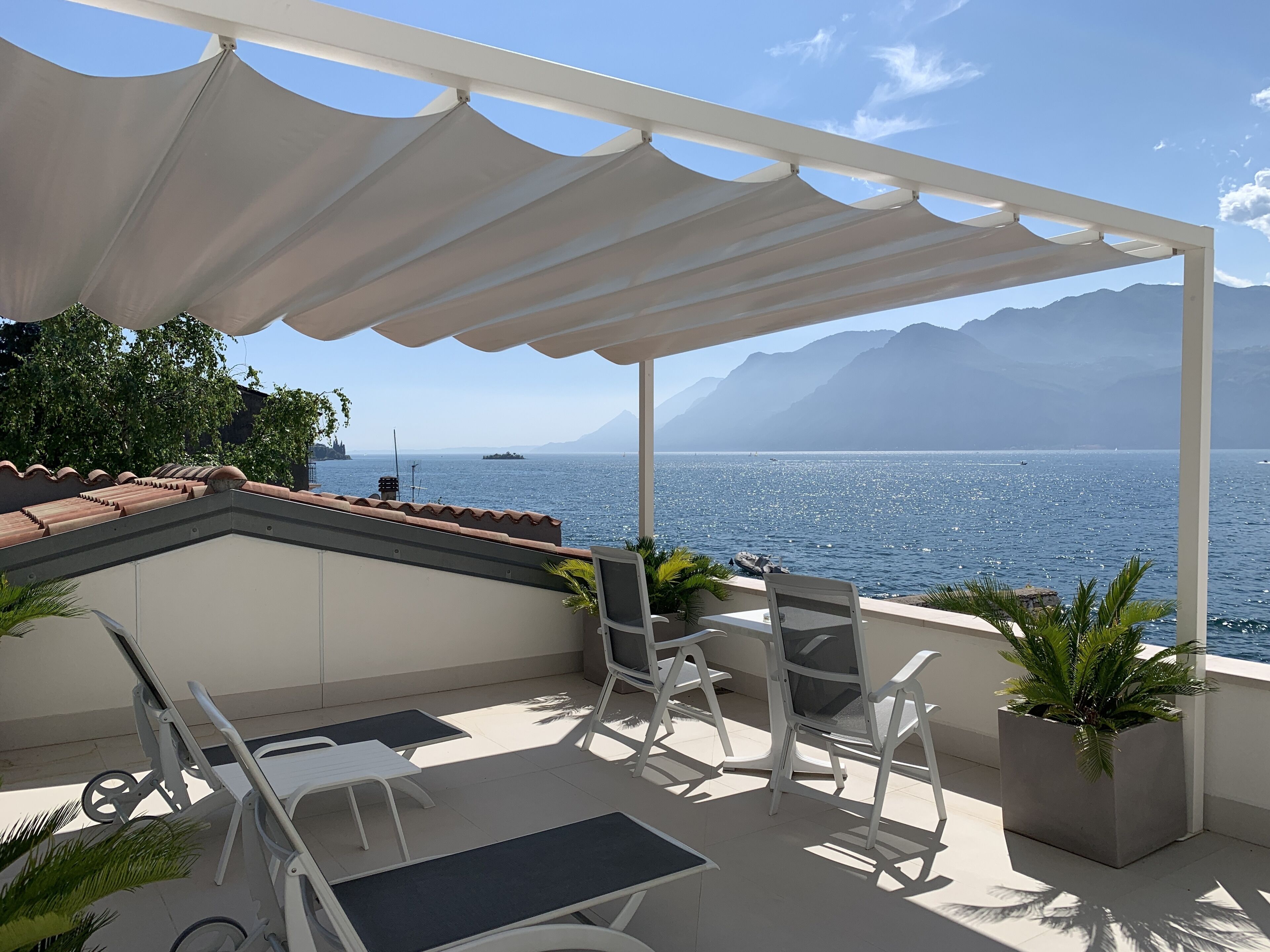 Una terraza con vistas al mar y a las montañas, que cuenta con mobiliario exterior y plantas en macetas.