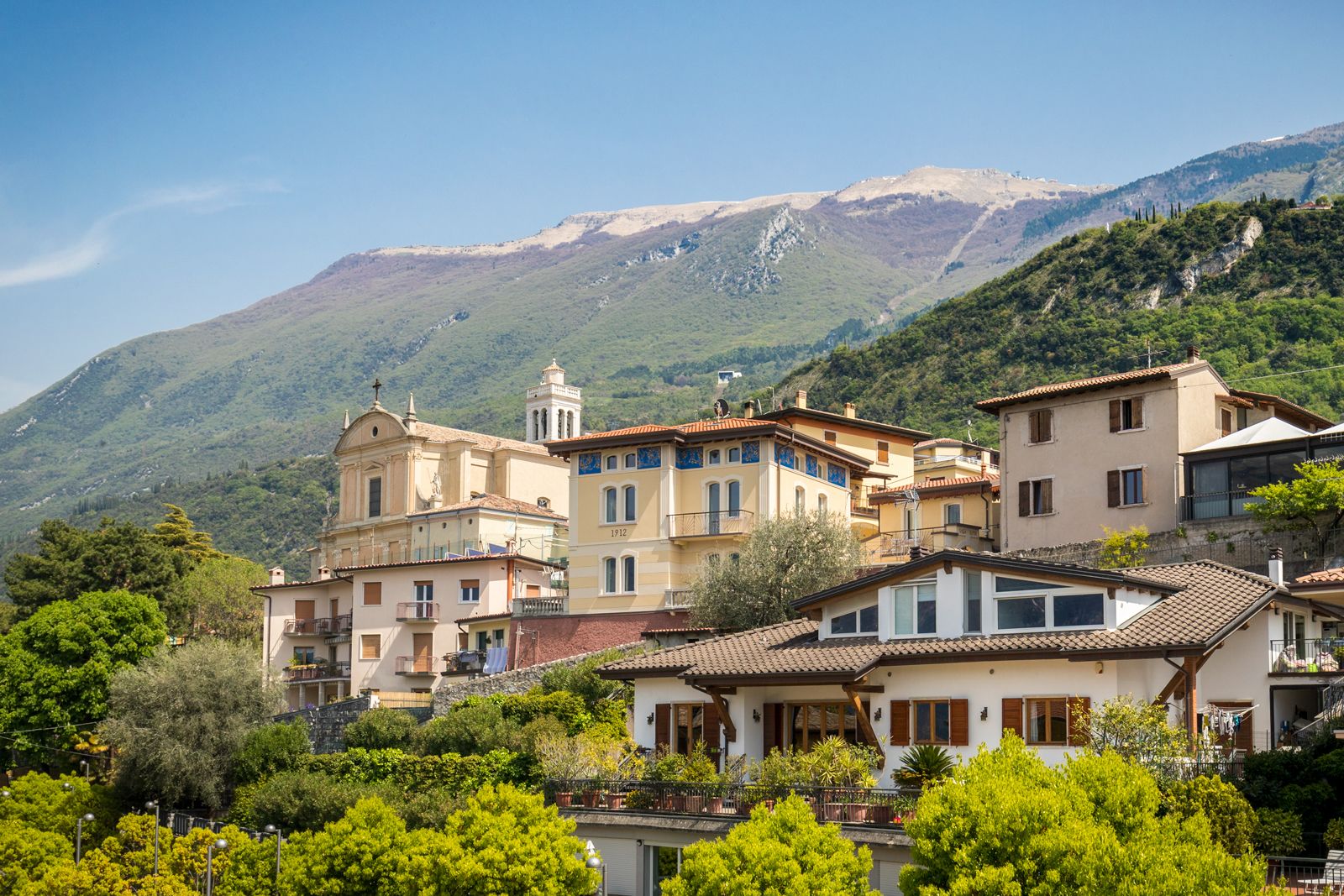 A hillside village with traditional Mediterranean architecture, including a church with a bell tower, and lush greenery.