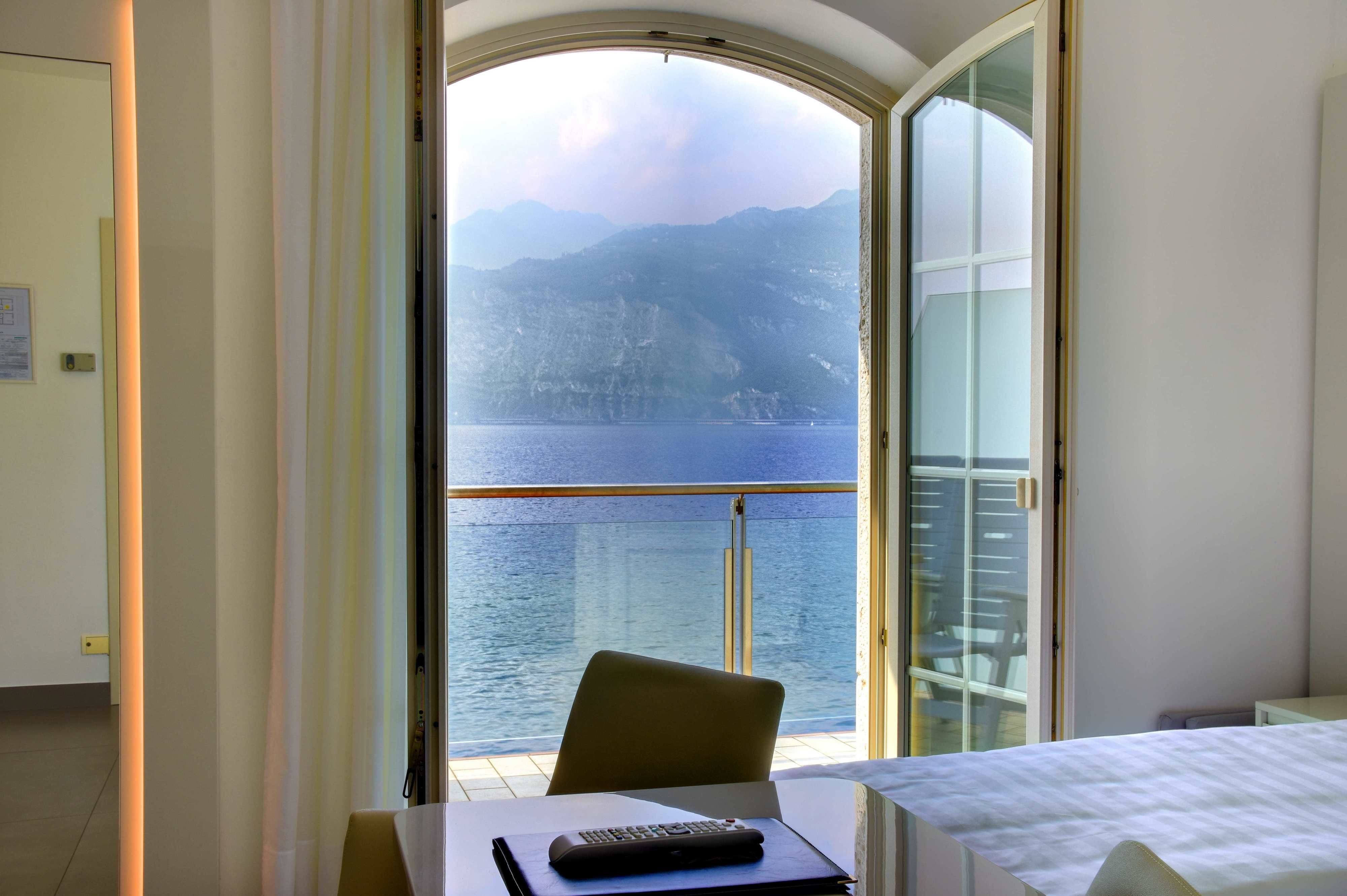 Une pièce avec vue sur un plan d’eau et des montagnes, comprenant une chaise, une table et un lit.