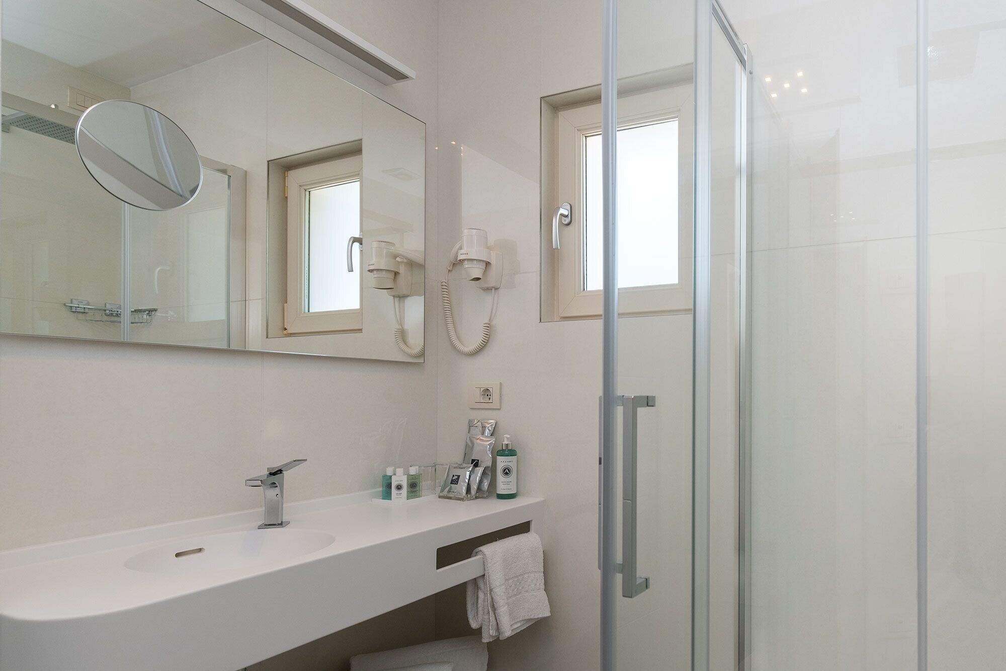 A modern bathroom with a glass shower enclosure, a white sink, and a large mirror.