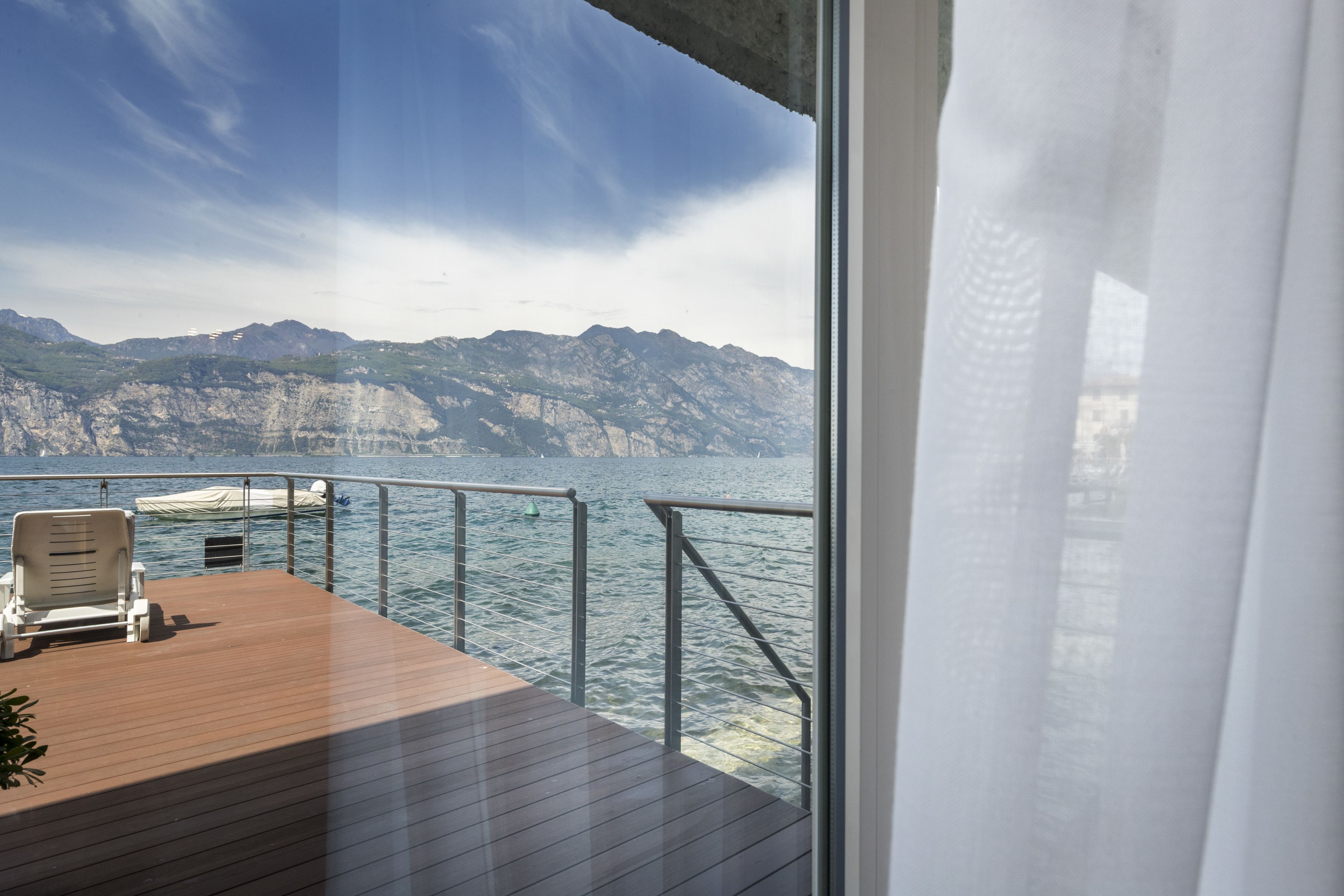 A deck with a chair and a boat, overlooking a body of water and mountains.