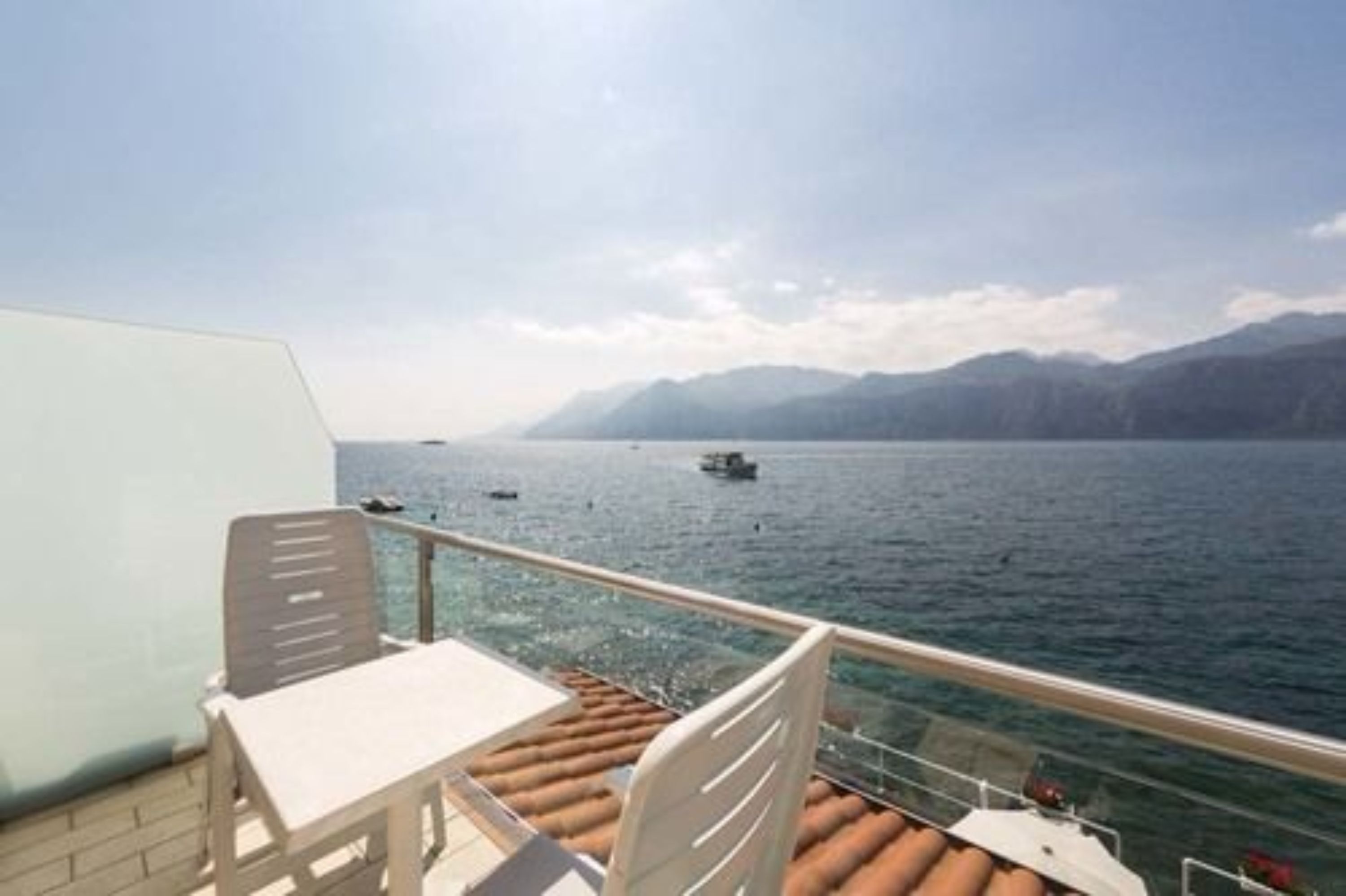 A deck with a table and chairs overlooking a body of water with boats and mountains in the distance.