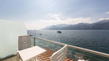 A deck with a table and chairs overlooking a body of water with boats and mountains in the distance.