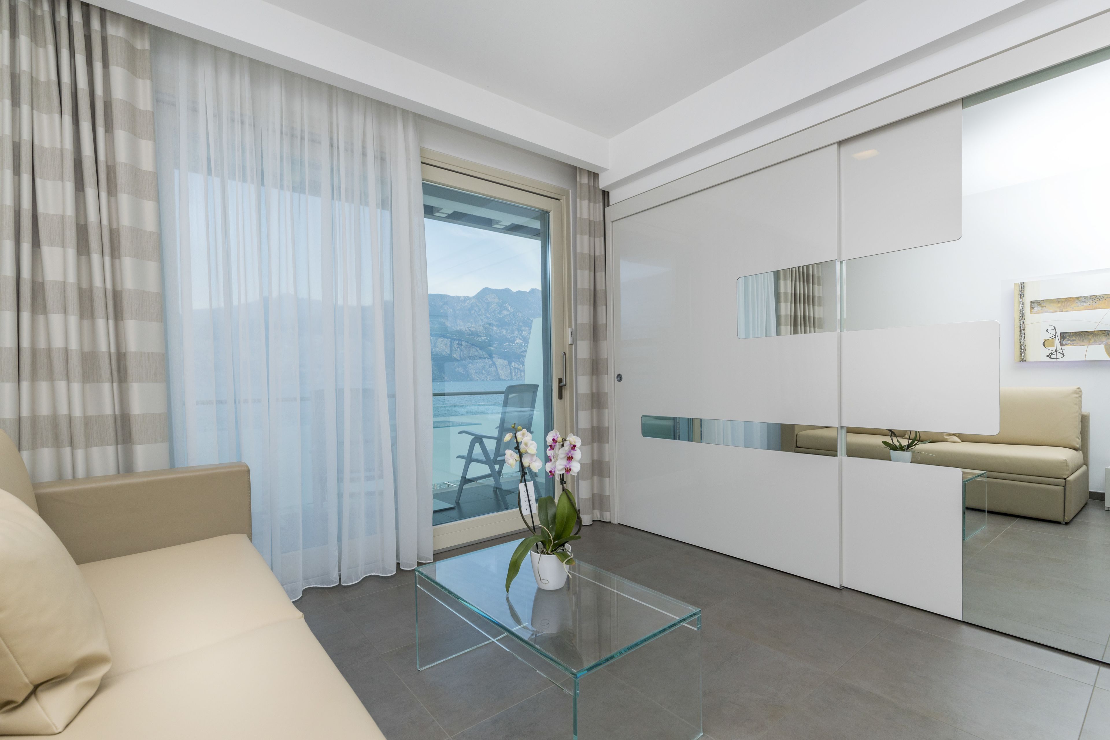 A modern living room with a glass coffee table, a sofa, and a view of mountains through a sliding glass door.