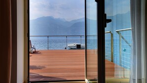 Une vue depuis un balcon doté d’une terrasse en bois, d’une balustrade, et donnant sur une étendue d’eau avec des montagnes en arrière-plan.