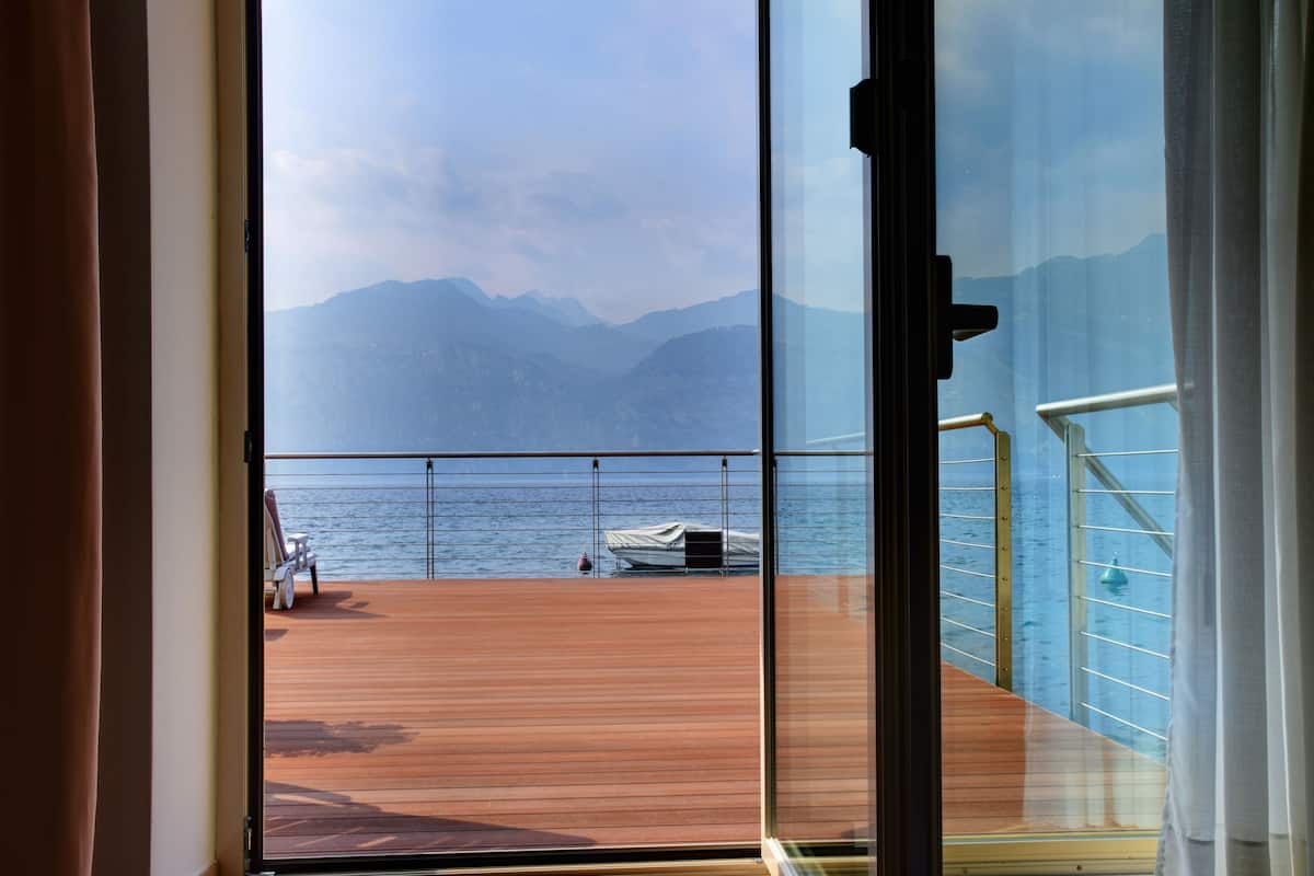 A view from a balcony with a wooden deck, a railing, and a body of water with mountains in the background.