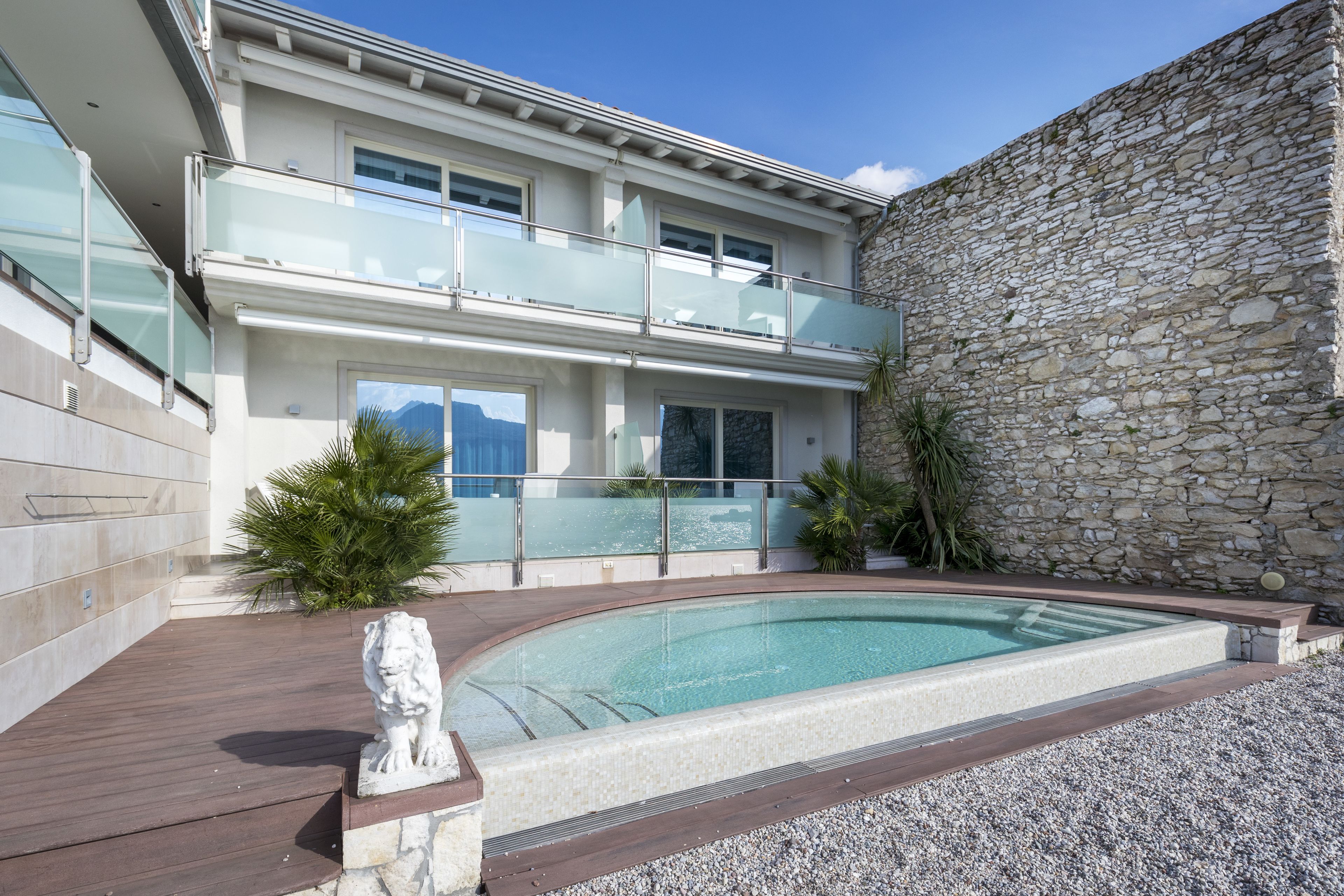 Una casa moderna de dos pisos con piscina, muro de piedra y balcón con barandillas de vidrio.