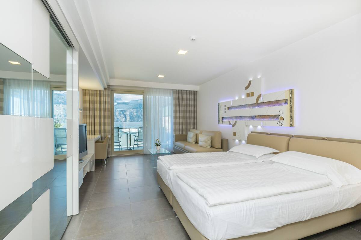 A modern hotel room with a large bed, a TV, a balcony with a view, and a dining area.