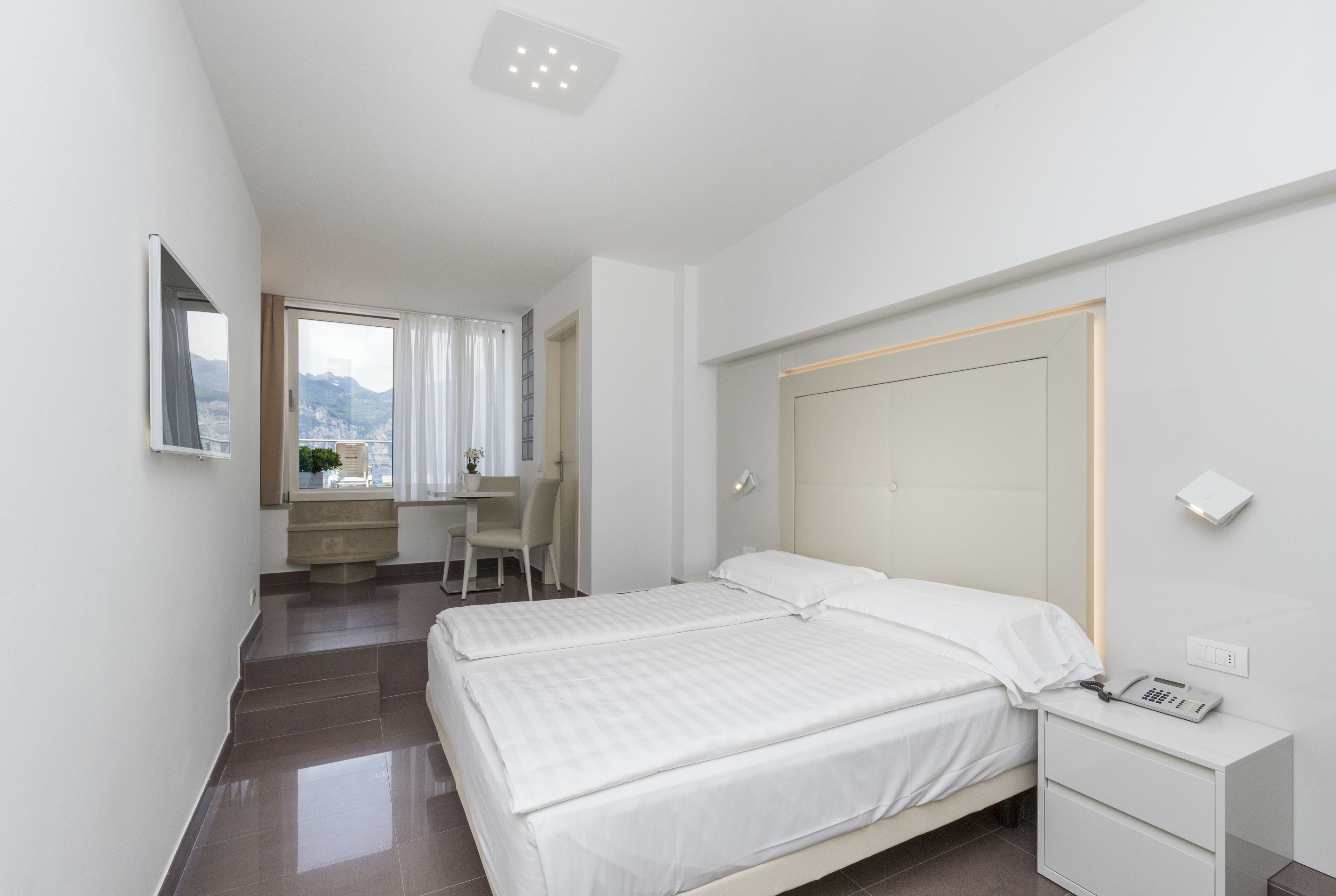 A modern hotel room with a large bed, a desk, and a view of the mountains.