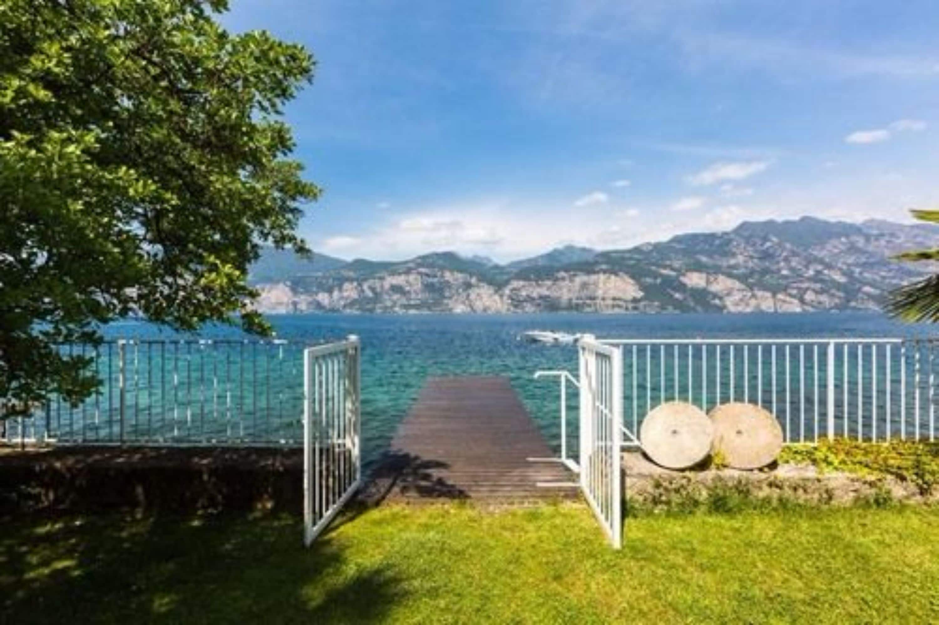Un muelle de madera que se extiende hacia un mar azul cristalino, con montañas al fondo.