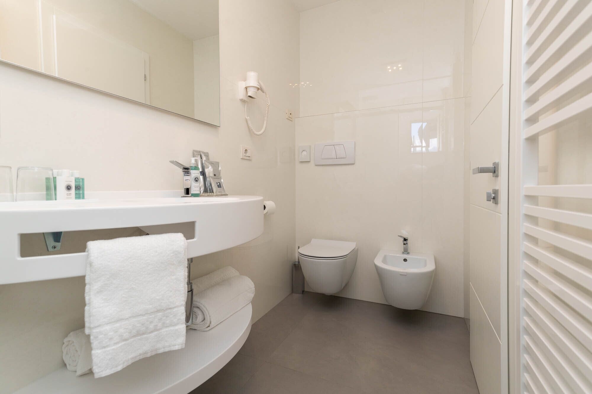 A modern bathroom with a white vanity, a toilet, a bidet, and a towel rack.
