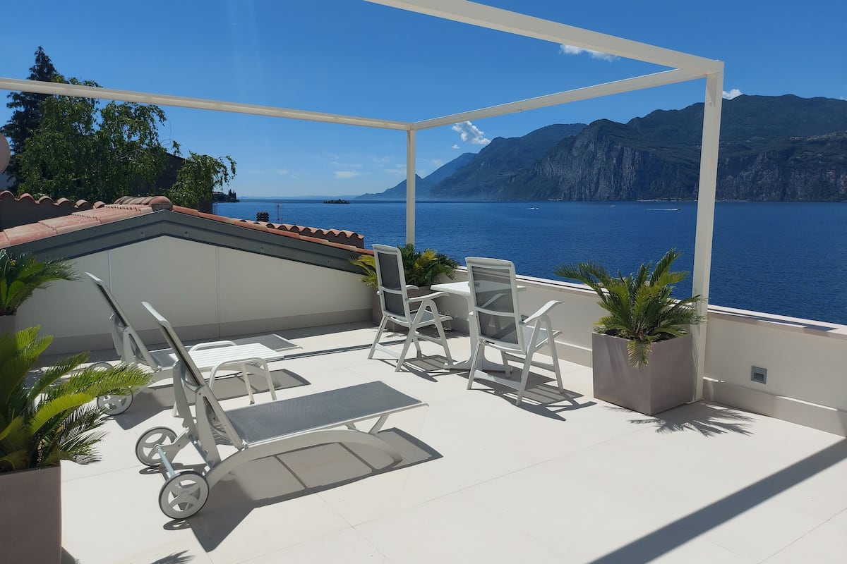 A terrace with a view of the sea and mountains, featuring a table and chairs, and a wheelchair.