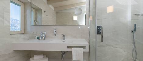 A modern bathroom with a large mirror, a white sink, and a glass-enclosed shower.
