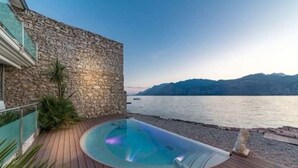Un bâtiment en pierre doté d’une terrasse en bois et d’une piscine, le tout surplombant une étendue d’eau.