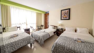 A hotel room with three beds, a desk, a chair, and a small table.