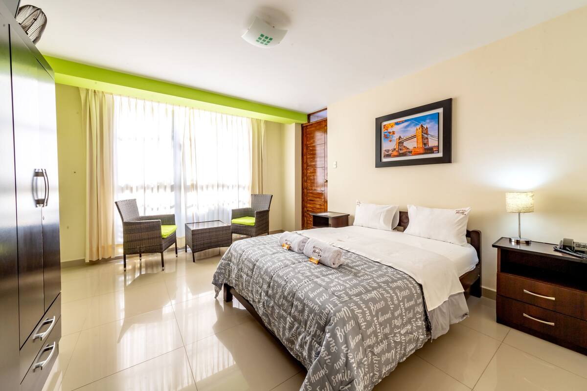 A hotel room with a bed, a desk, a chair, a nightstand, and a picture on the wall.