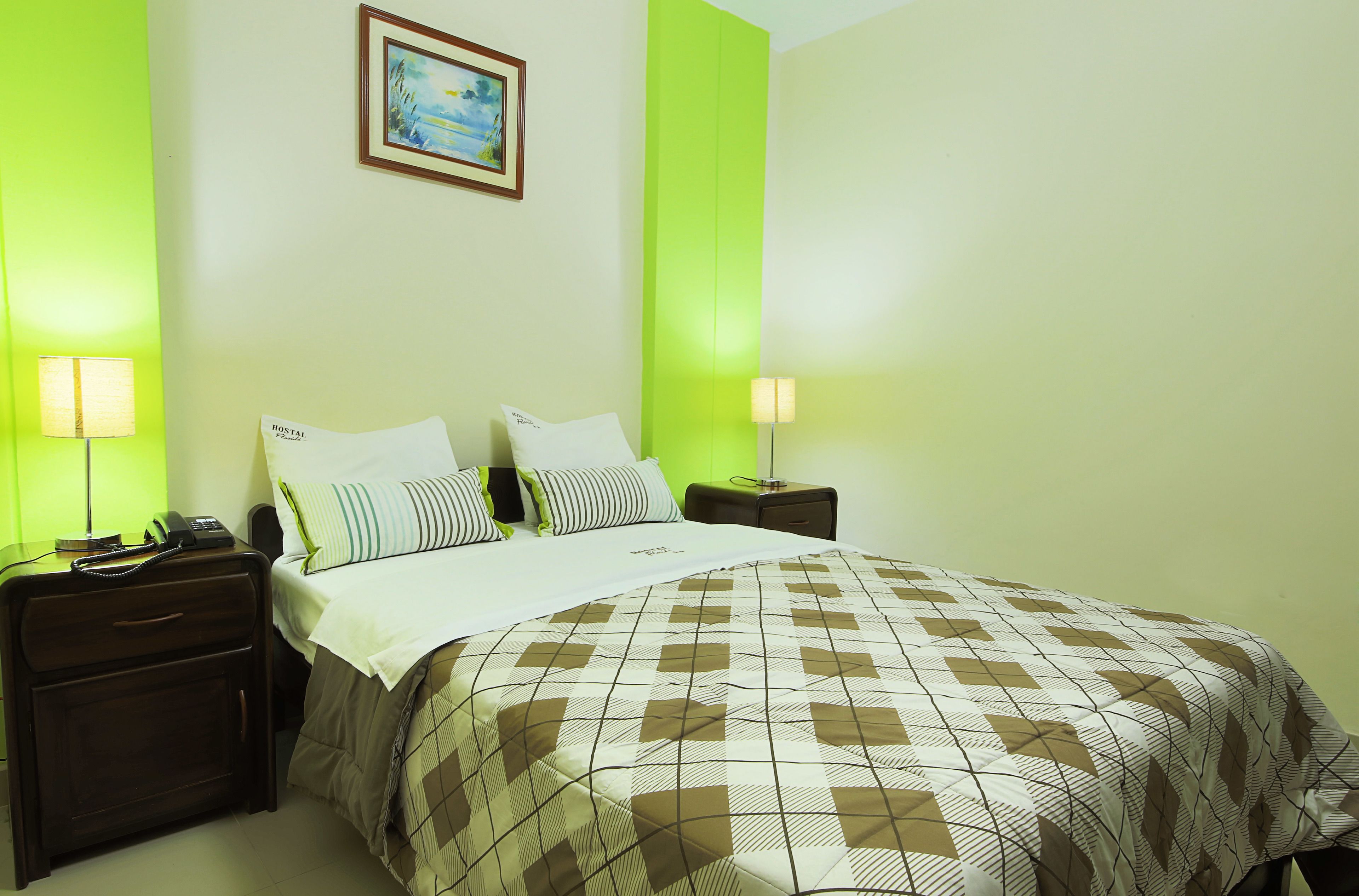 A hotel room with a bed, two bedside tables, a nightstand, a lamp, and a framed picture on the wall.