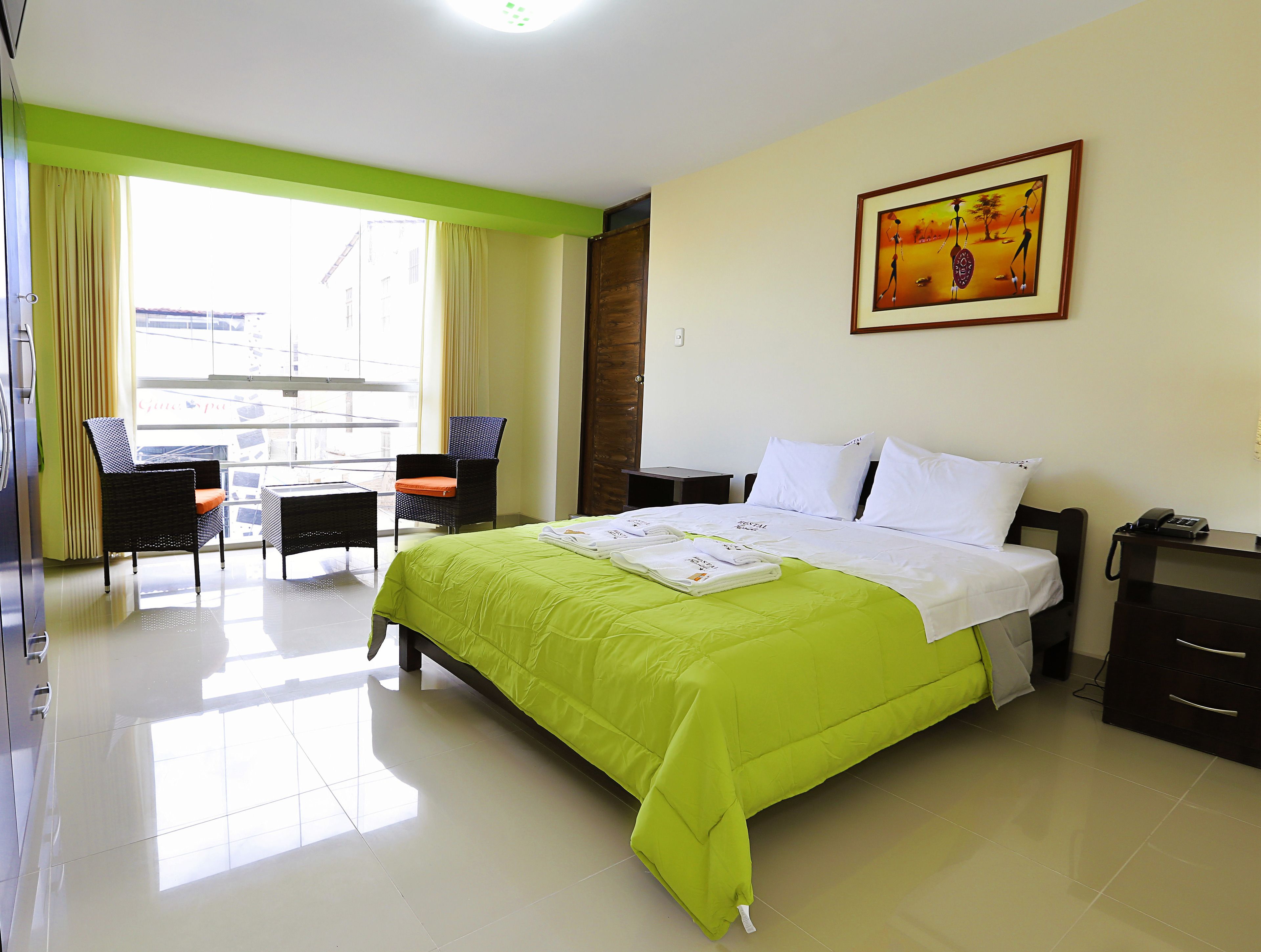 A hotel room with a bed, a chair, a table, and a painting on the wall.