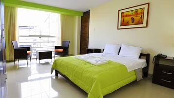 A hotel room with a bed, a chair, a table, and a painting on the wall.