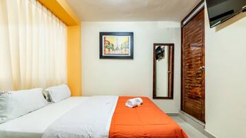A hotel room with a bed, a wooden wardrobe, a framed picture on the wall, and a TV mounted above the wardrobe.