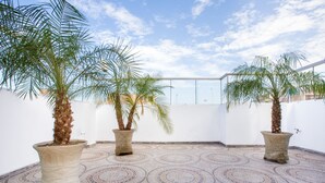 A rooftop terrace with three large potted palm trees, a patterned tiled floor, and a clear sky. - Hostal Florida (Chiclayo)
