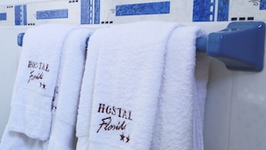 Three white towels with "HOSTAL Florida" text hanging on a blue towel rack in a bathroom with blue and white tiled walls. - Hostal Florida (Chiclayo)