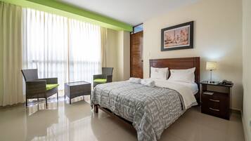 Quarto de hotel com cama, duas cadeiras, mesa de cabeceira e um quadro na parede.