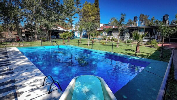 Une piscine dotée d’une terrasse en bois et d’une échelle, entourée d’une pelouse et d’arbres.