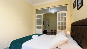Ein ordentlich bezogenes Bett mit weißen Leinen und einer grünen Tagesdecke, ein braunes Polsterkopfstück und eine Tür zu einem Badezimmer.