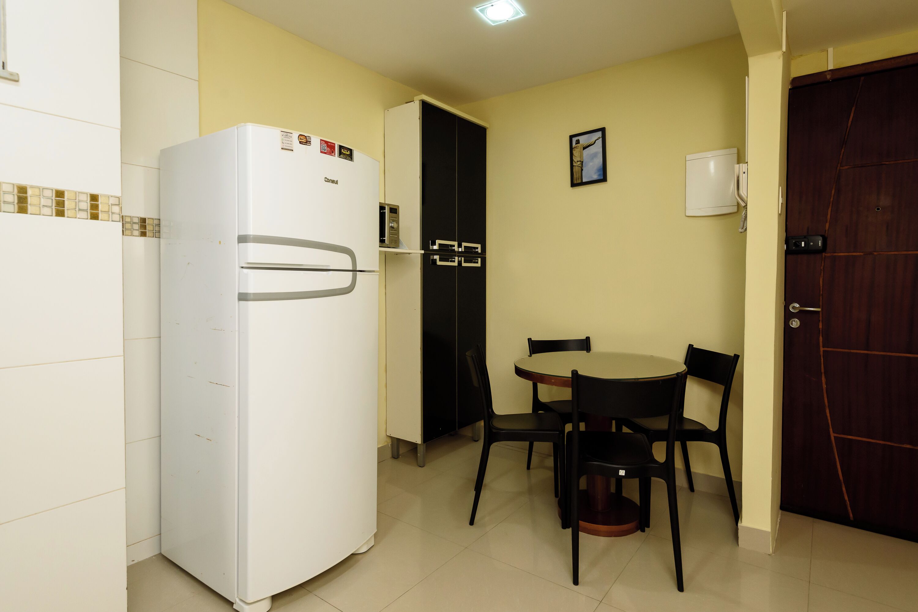 Una cocina compacta con refrigerador, un mueble negro, una mesa de comedor con cuatro sillas y una puerta de madera.