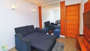 A living room with a sofa, ottomans, a wooden door, and a mirror reflecting the room. - MZ Apartments Prado I (Rio de Janeiro)