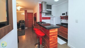 A modern kitchen with a central island, red bar stools, a gas stove, and a microwave. - MZ Apartments Prado I (Rio de Janeiro)