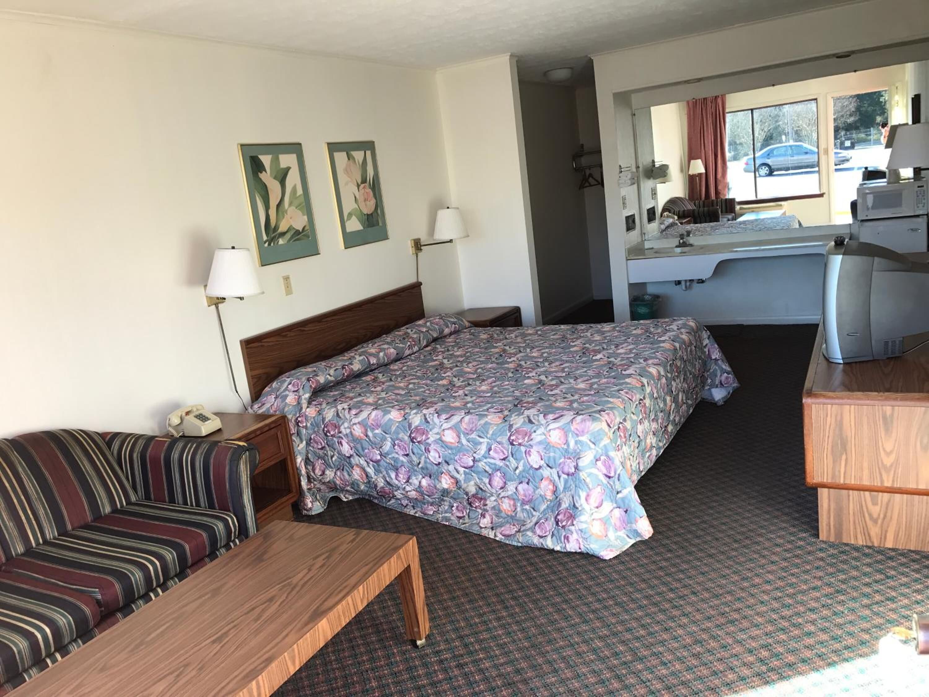 Hotellihuone, jossa on sänky, sohva, työpöytä ja pieni keittiönurkkaus.