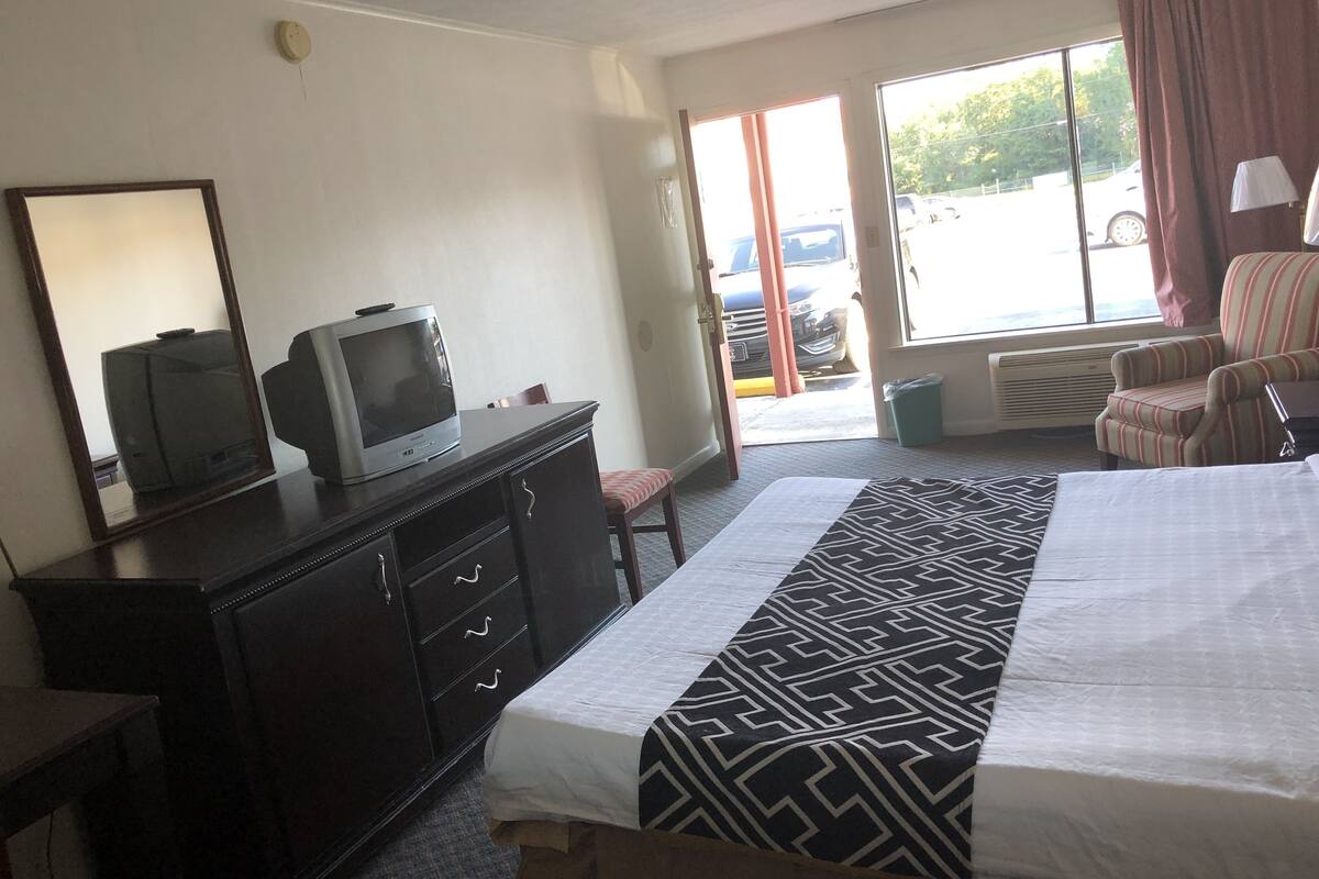 Habitación de hotel con cama, cómoda, televisor, ventana con vista a un estacionamiento y un sillón a rayas.