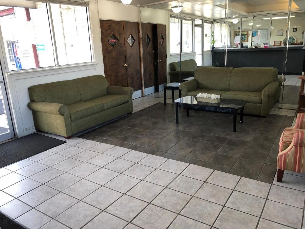A hotel lobby with a green sofa, a coffee table, and a striped armchair. There are wooden doors and a reception desk in the background.