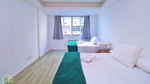 A hotel room with a bed, a bench, a window with curtains, and a view of buildings outside. - MZ Apartments Prado Junior (Rio de Janeiro)