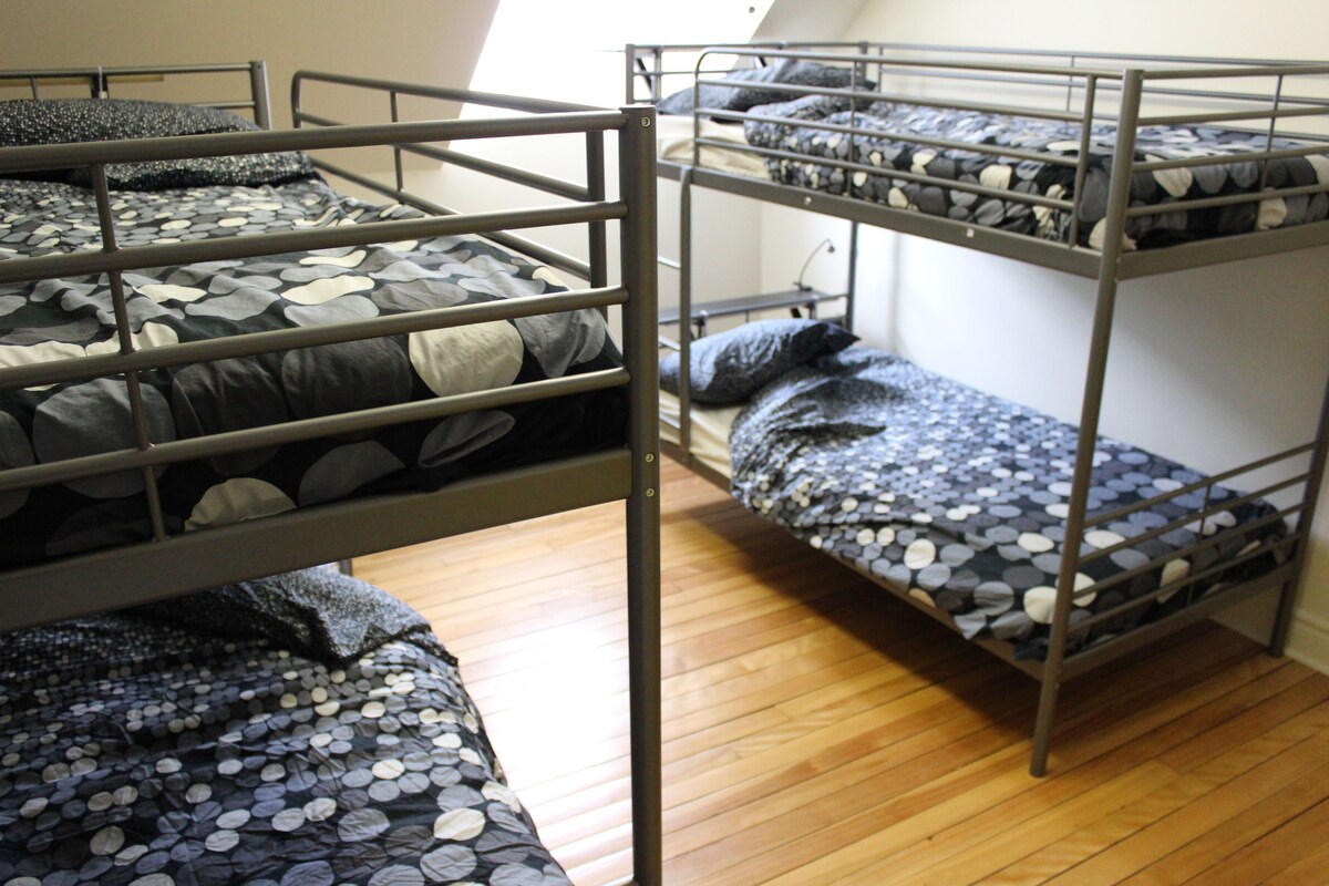 A dormitory room with bunk beds, wooden flooring, and a window providing natural light.