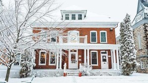 A two-story brick house with a white porch and a snow-covered landscape. - Auberge Jeunesse Magog-Orford (Hostel) (Magog)
