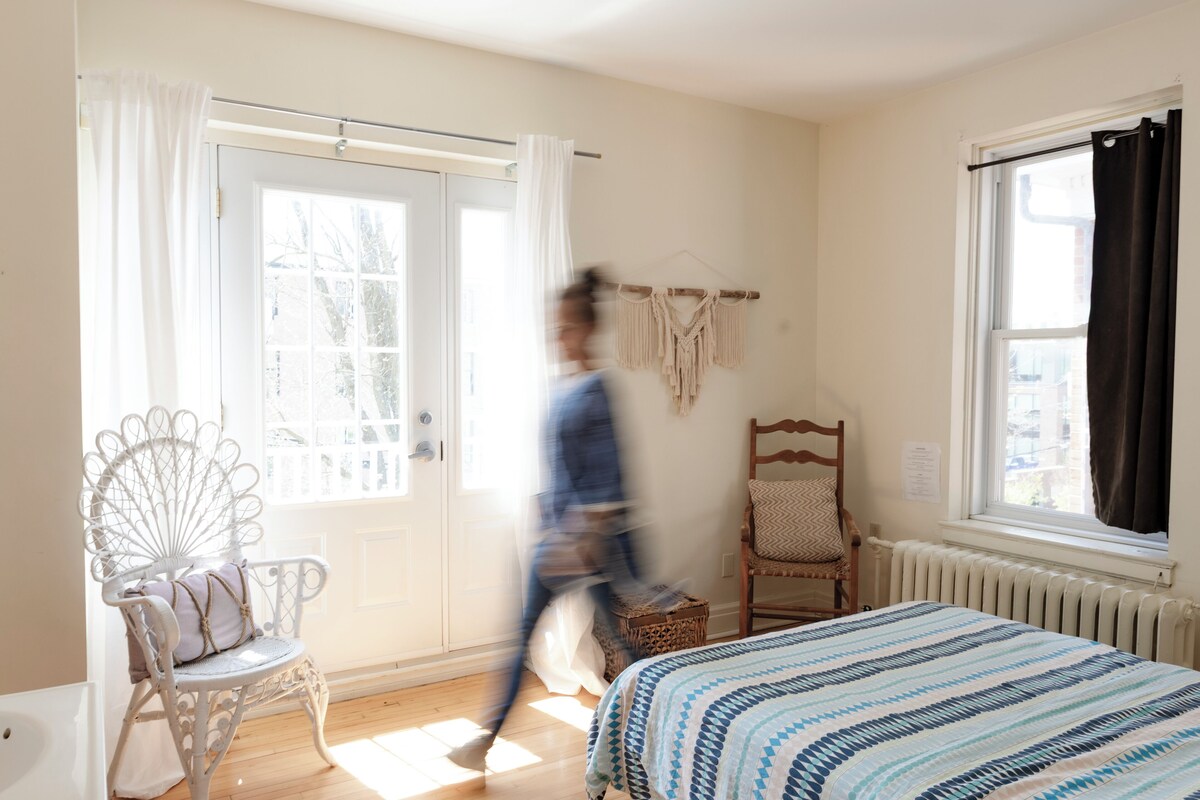 A room with a bed, a chair, a window, and a door.