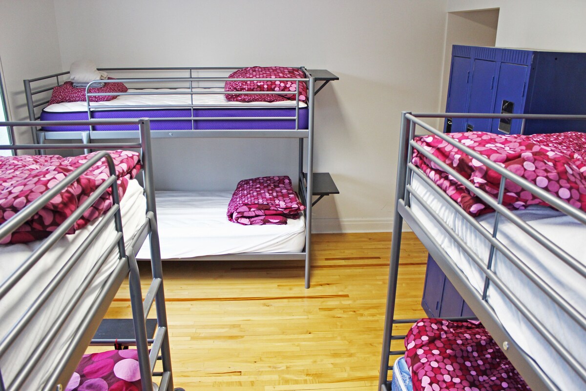 A dormitory room with bunk beds, wooden flooring, and blue lockers.