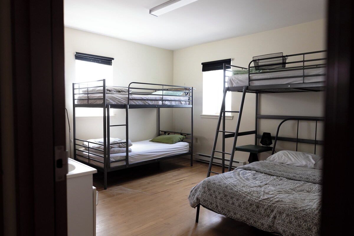 A dormitory room with bunk beds, a desk, and a window.