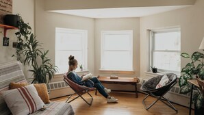 A cozy living room with a person reading, large windows, a sofa, and two chairs. - Auberge Jeunesse Magog-Orford (Hostel) (Magog)