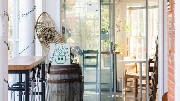 A cafe with a wooden sign reading "Cafe Les Estries" and a rustic interior with a wooden barrel, metal chairs, and a table. - Auberge Jeunesse Magog-Orford (Hostel) (Magog)