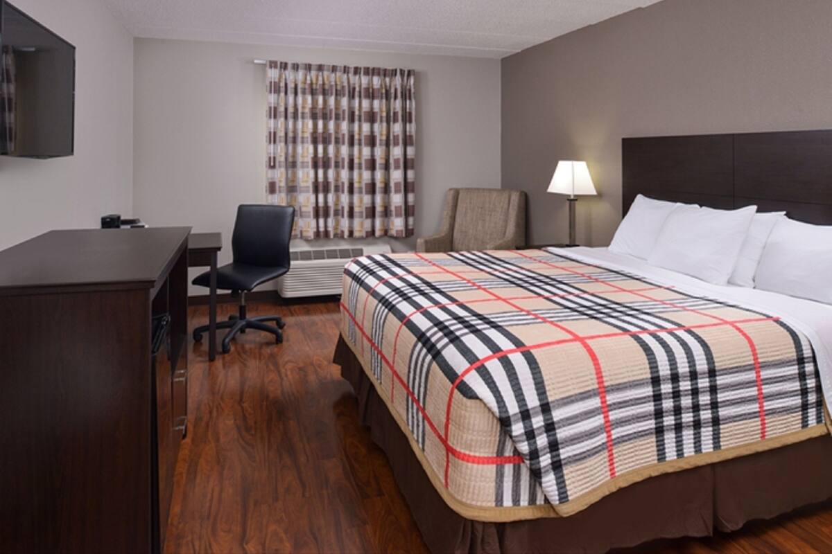 A hotel room with a large bed, a desk, a chair, a TV, a window with curtains, and a lamp.